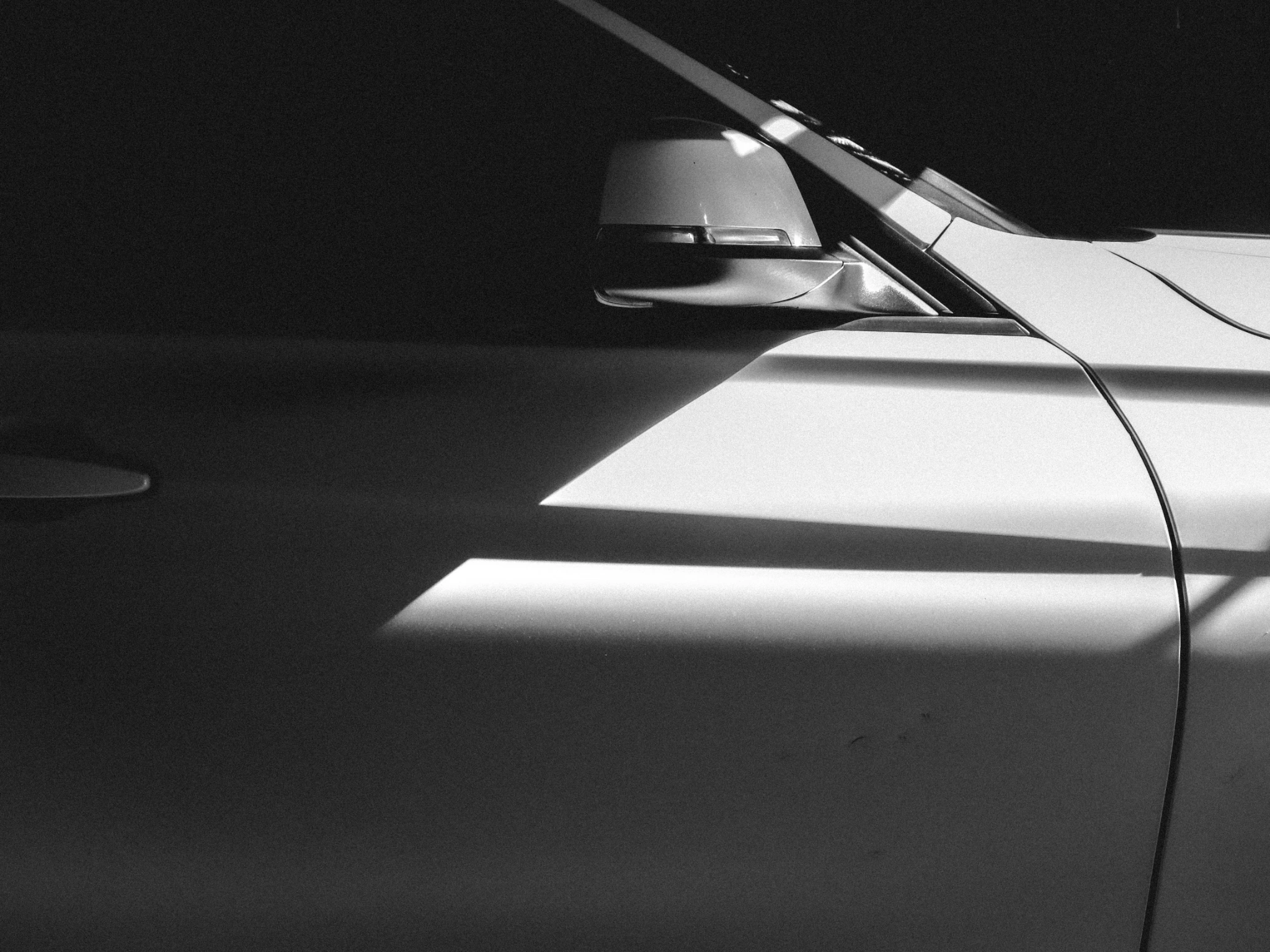 Light and shadow across a vehicle door and side mirror, photographed in black and white.