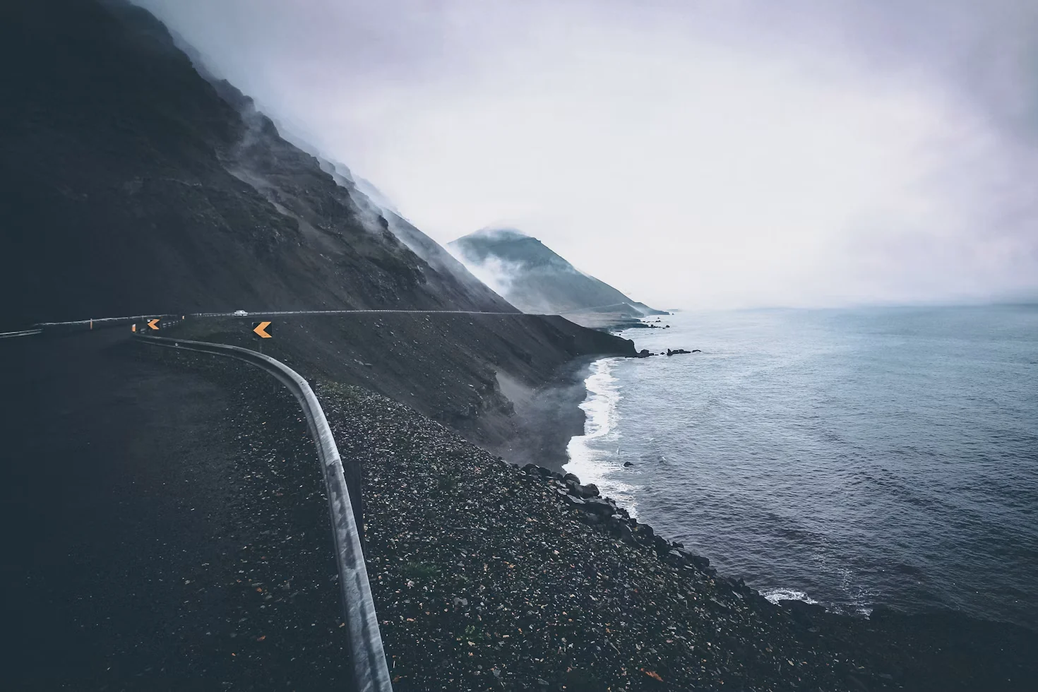 A coastal road curves along a dark mountainside above the sea.