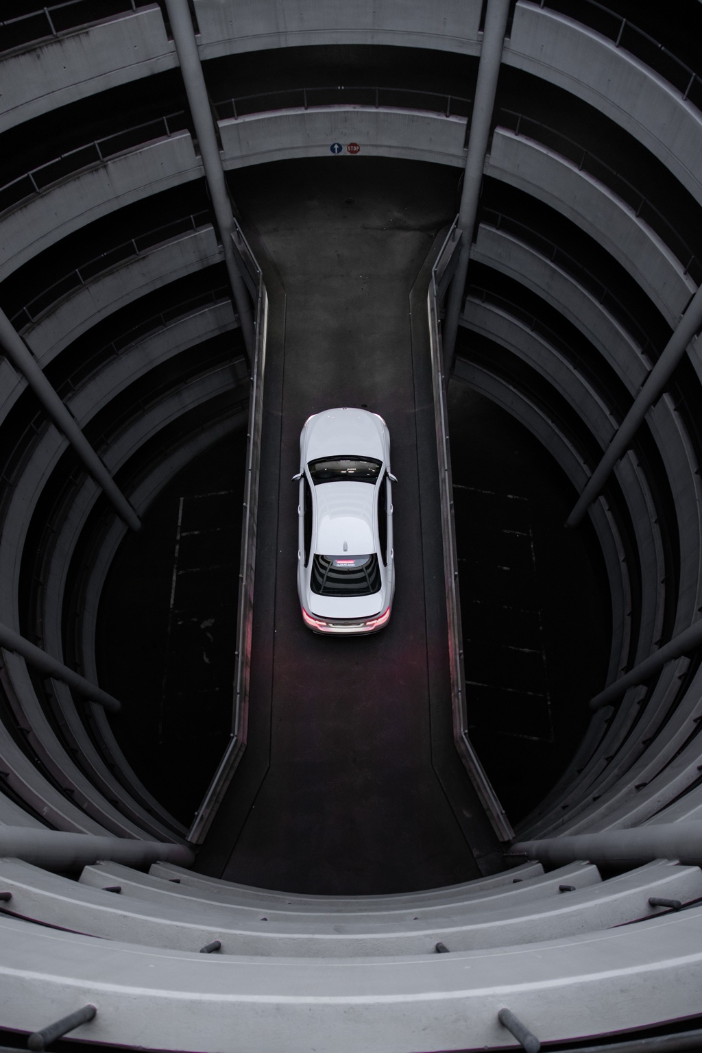 Overhead view of a white vehicle between the curved ramps of a parking structure.