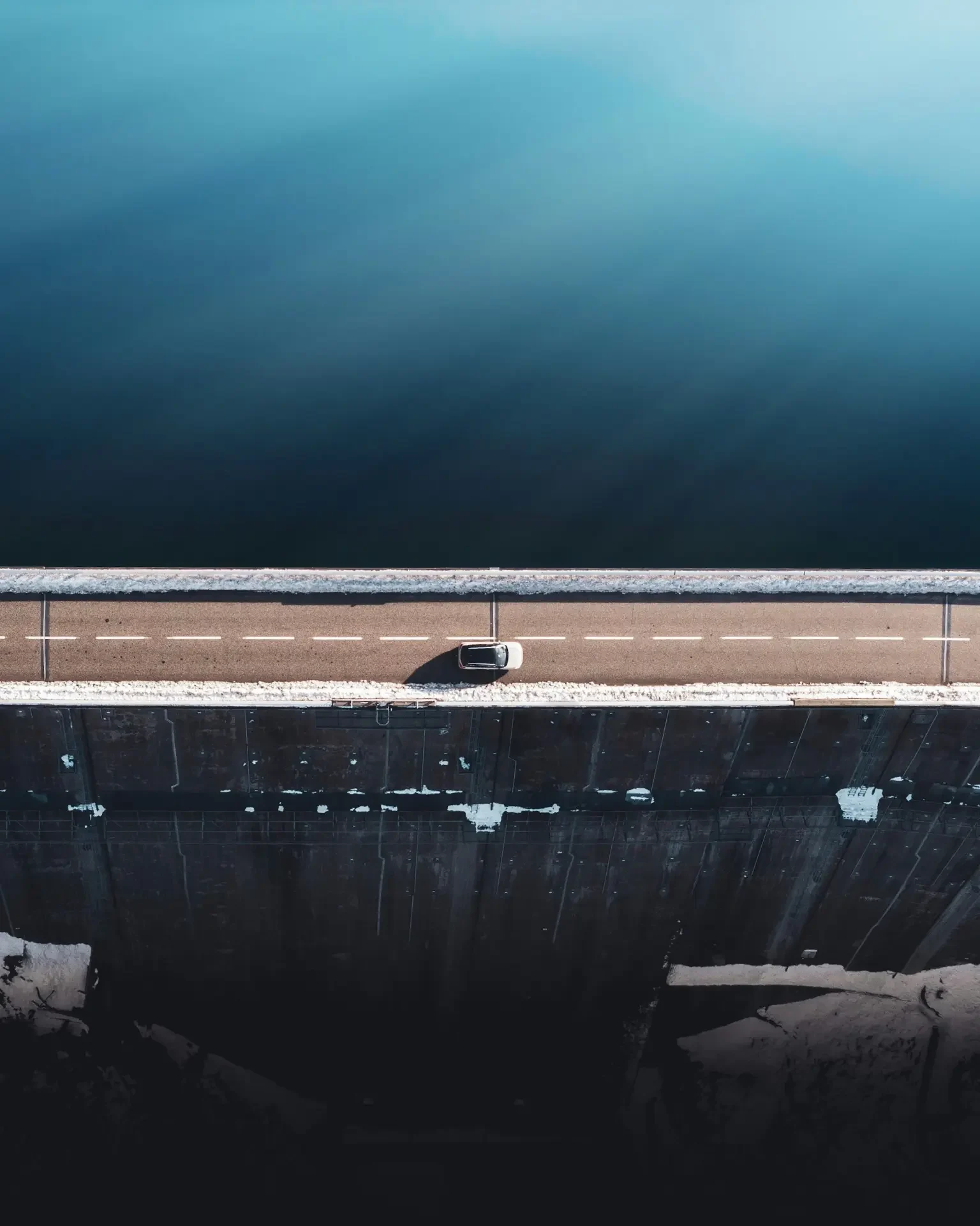 Aerial view of a vehicle on a road beside deep blue water.